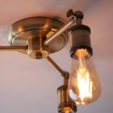 Close-up of Endon Brackley 3 light semi-flush ceiling light in brass, showing the central mount, adjustable arms, and an exposed E27 filament bulb.