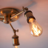 Close-up of Endon Brackley semi-flush ceiling light in brass, showing an adjustable arm with knurled E27 lamp holder and lit teardrop filament bulb.
