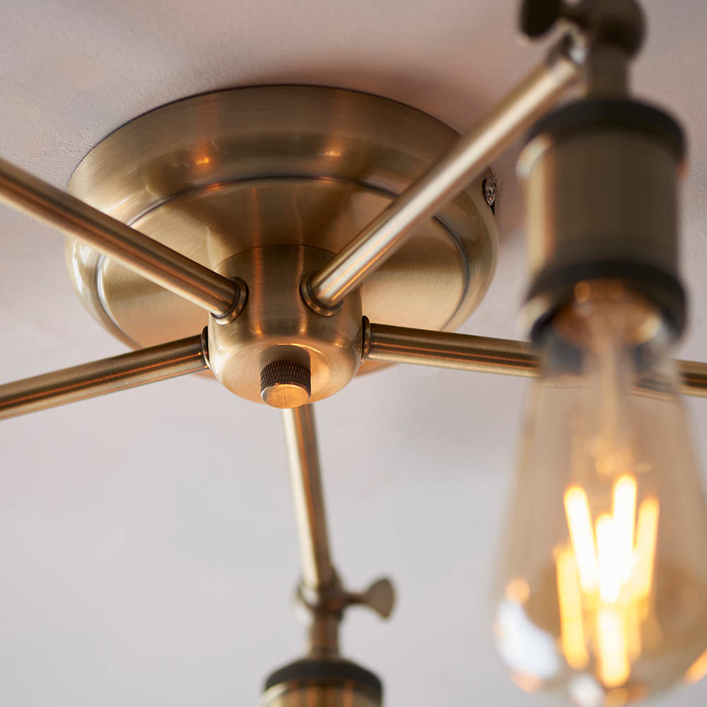 Close-up of the Brackley 5 Light Semi-Flush Ceiling Light in brass, showing metal arms, E27 bulb, and ceiling mount detail.