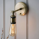Antique brass Brackley wall light with adjustable arm, knurled knob, and E27 fitting, shown lit with an exposed filament bulb.
