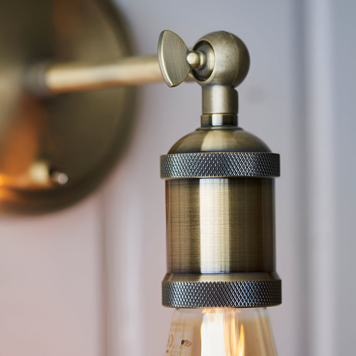 Close-up of the antique brass Brackley Wall Light showing the knurled E27 bulb holder, adjustable ball joint, and wing-nut control.