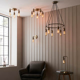 Brackley Table Lamp in brass, adjustable industrial-style design with knuckle joint and exposed bulb, shown on a side table beside an armchair in a living room.
