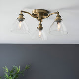 Wentworth 3 Light Semi-Flush Ceiling Light in antique brass with three angled arms and clear dome glass shades, shown against a white ceiling and grey wall.
