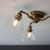 Wentworth 3 Light Semi-Flush Ceiling Light in antique brass, curved arms holding clear glass bell shades with visible bulbs, mounted on a round ceiling plate.