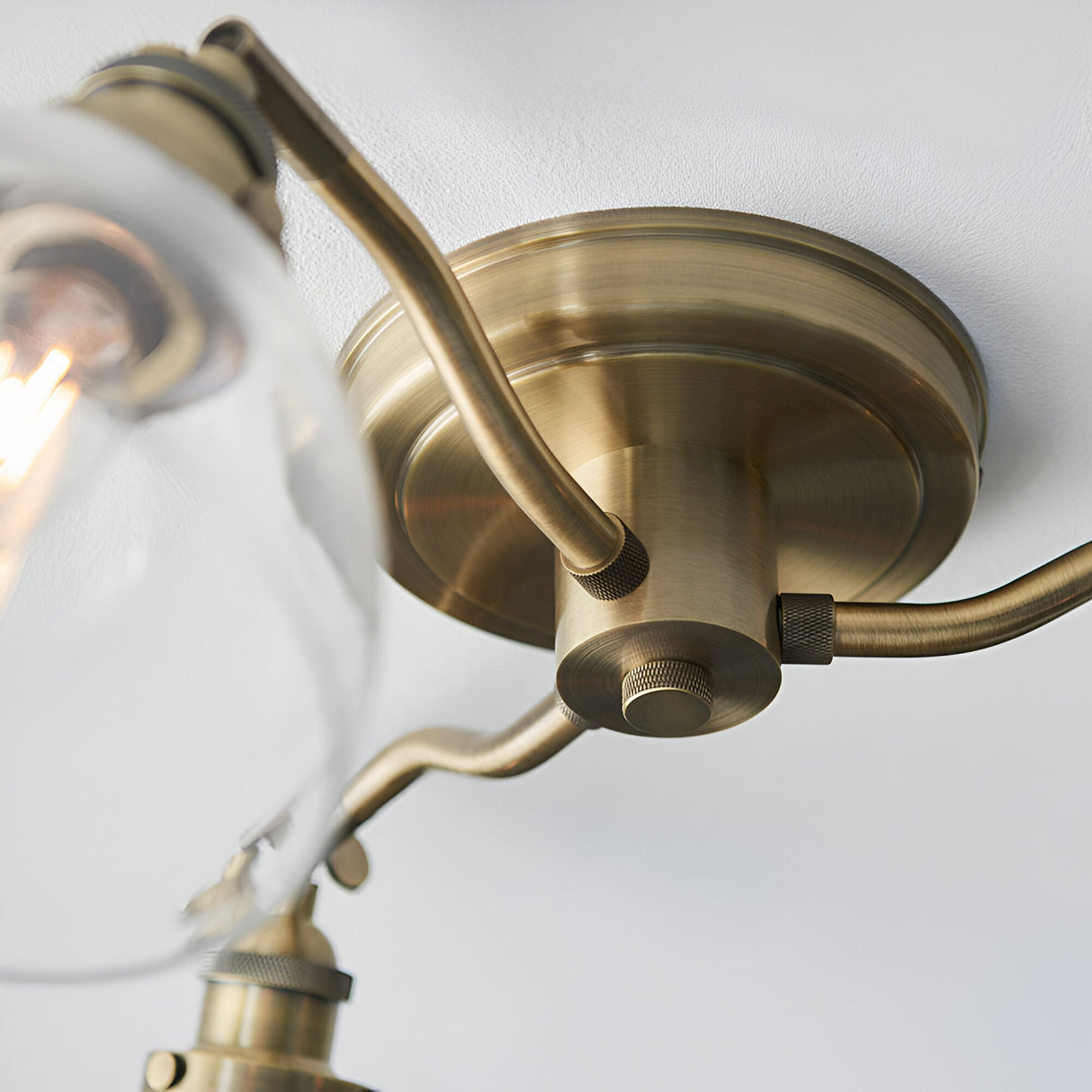 Close-up of the Wentworth 3-light semi-flush ceiling light in antique brass, showing the ceiling plate, angled arms, and glass shade fitting.