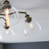 Close-up of Endon Wentworth semi-flush ceiling light in antique brass with clear glass dome shades and lit E14 filament bulbs.