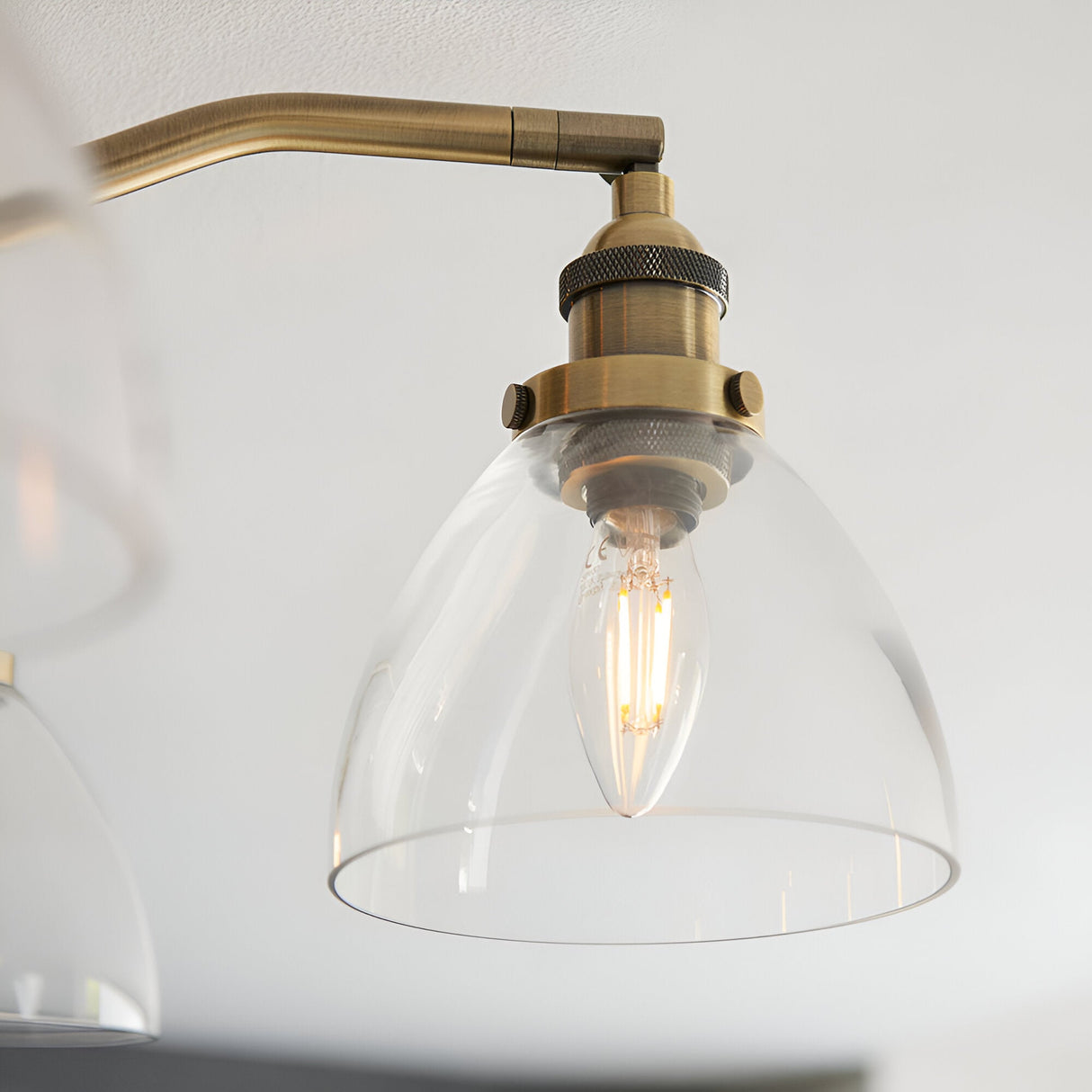 Close-up of the Endon Wentworth semi-flush ceiling light showing an antique brass arm, dome-shaped clear glass shade, and lit E14 filament candle bulb.