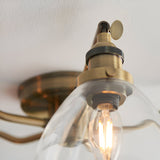 Close-up of Endon Wentworth semi-flush ceiling light showing antique brass fitting, knurled detail and lit E14 candle bulb within a clear glass shade.