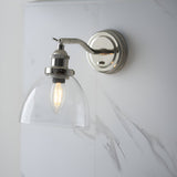 Endon Wentworth adjustable wall light in nickel with knurled lamp holder, clear glass dome shade and lit E14 filament bulb, on a marble wall.