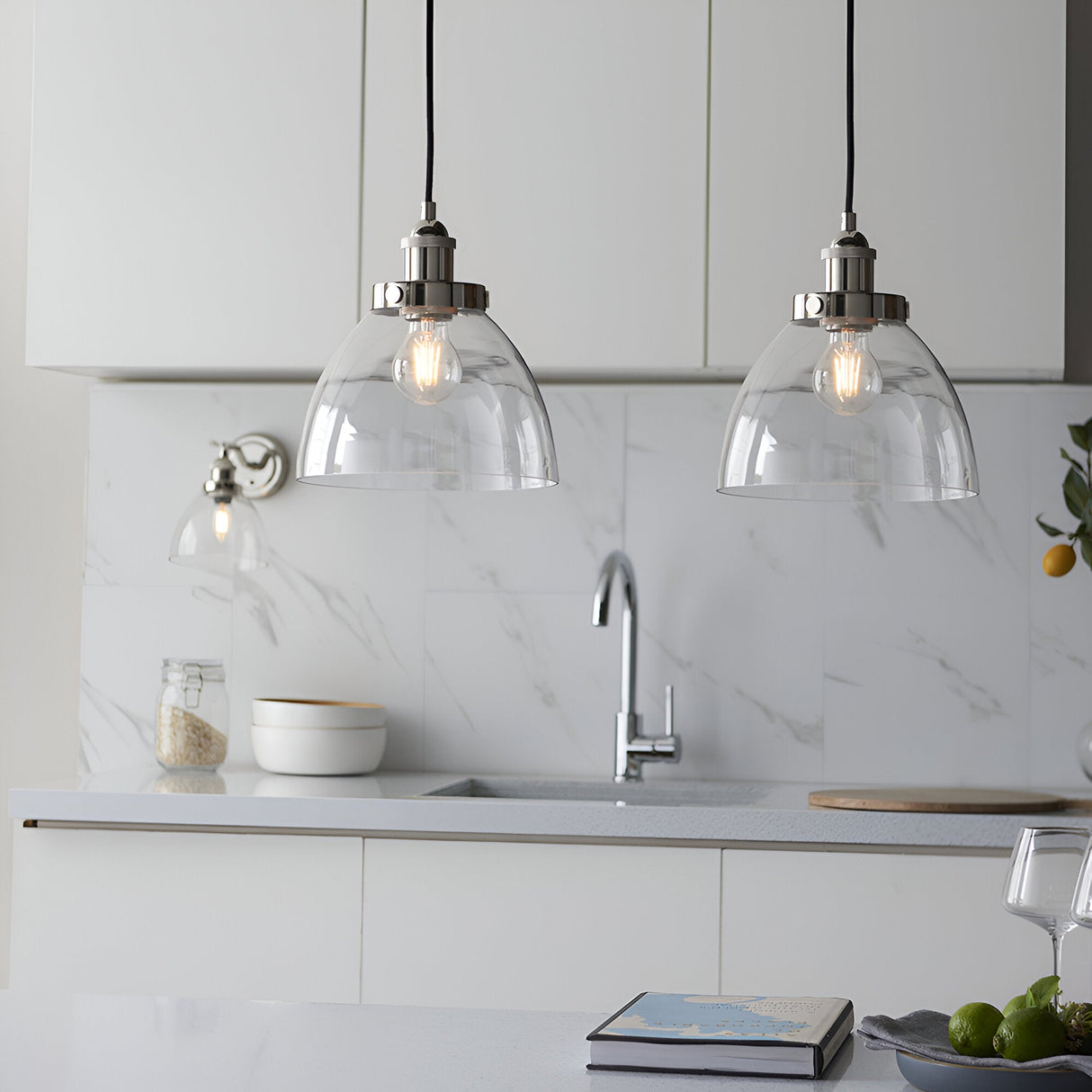Endon Wentworth nickel wall light with clear glass shade beside two matching pendant lights over a white marble kitchen sink area.