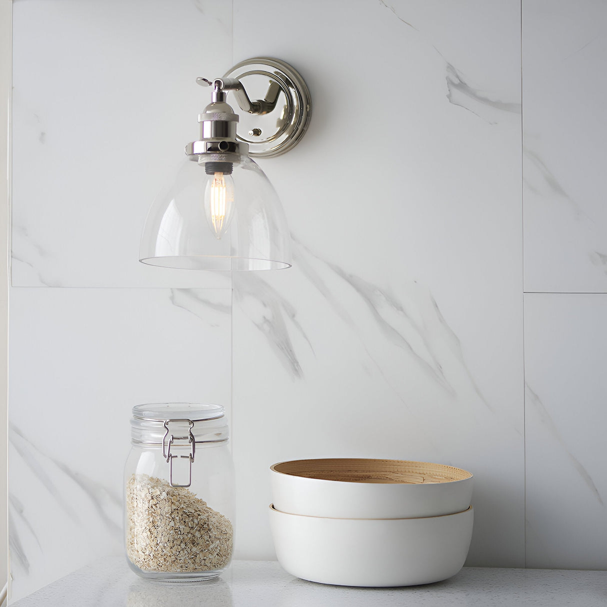 Endon Wentworth adjustable wall light in nickel with clear glass bell shade and E14 filament bulb, mounted on a marble wall above a jar and bowls.