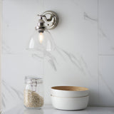 Endon Wentworth adjustable wall light in nickel with clear glass bell shade and E14 filament bulb, mounted on a marble wall above a jar and bowls.