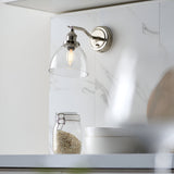 Endon Wentworth adjustable wall light in nickel with clear glass dome shade and E14 filament bulb, mounted on a marble kitchen wall above a shelf.