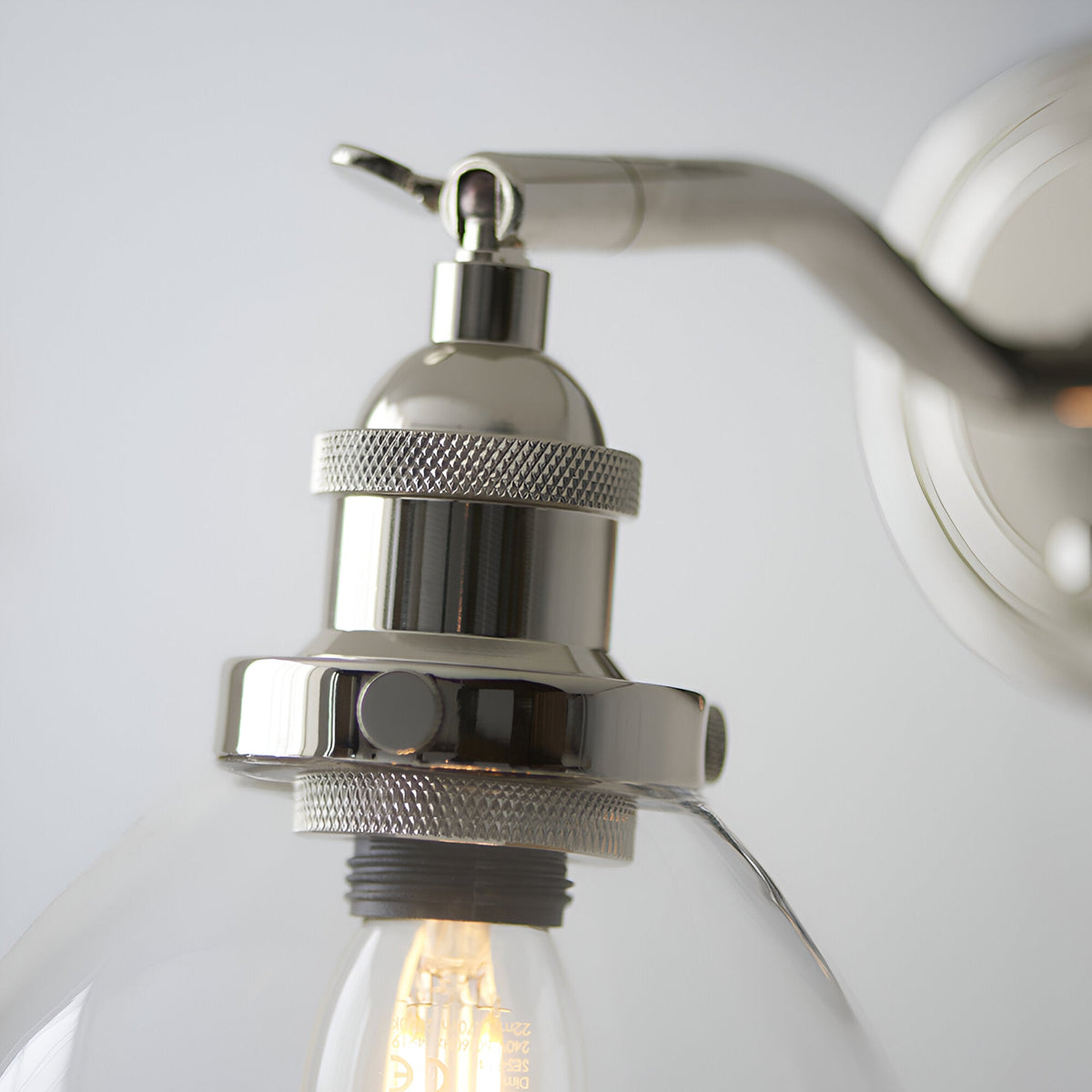 Close-up of Endon Wentworth wall light in nickel, showing knurled E14 lamp holder, adjustable knuckle, toggle switch and clear glass shade with filament bulb.