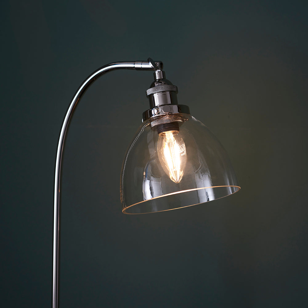 Endon Wentworth table lamp in nickel with clear glass dome shade, knurled lamp holder, adjustable knuckle and lit E14 filament bulb against a dark background.