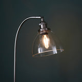 Endon Wentworth table lamp in nickel with clear glass dome shade, knurled lamp holder, adjustable knuckle and lit E14 filament bulb against a dark background.
