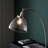 Endon Wentworth nickel floor lamp with arched arm, knurled holder and clear glass shade over an E27 filament bulb, set against a dark green wall.