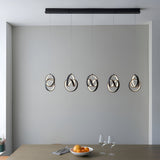 Bevwell 5 light linear pendant in matt black metal, looped ring designs with integrated LEDs, hung above a dining table in a grey-walled room.