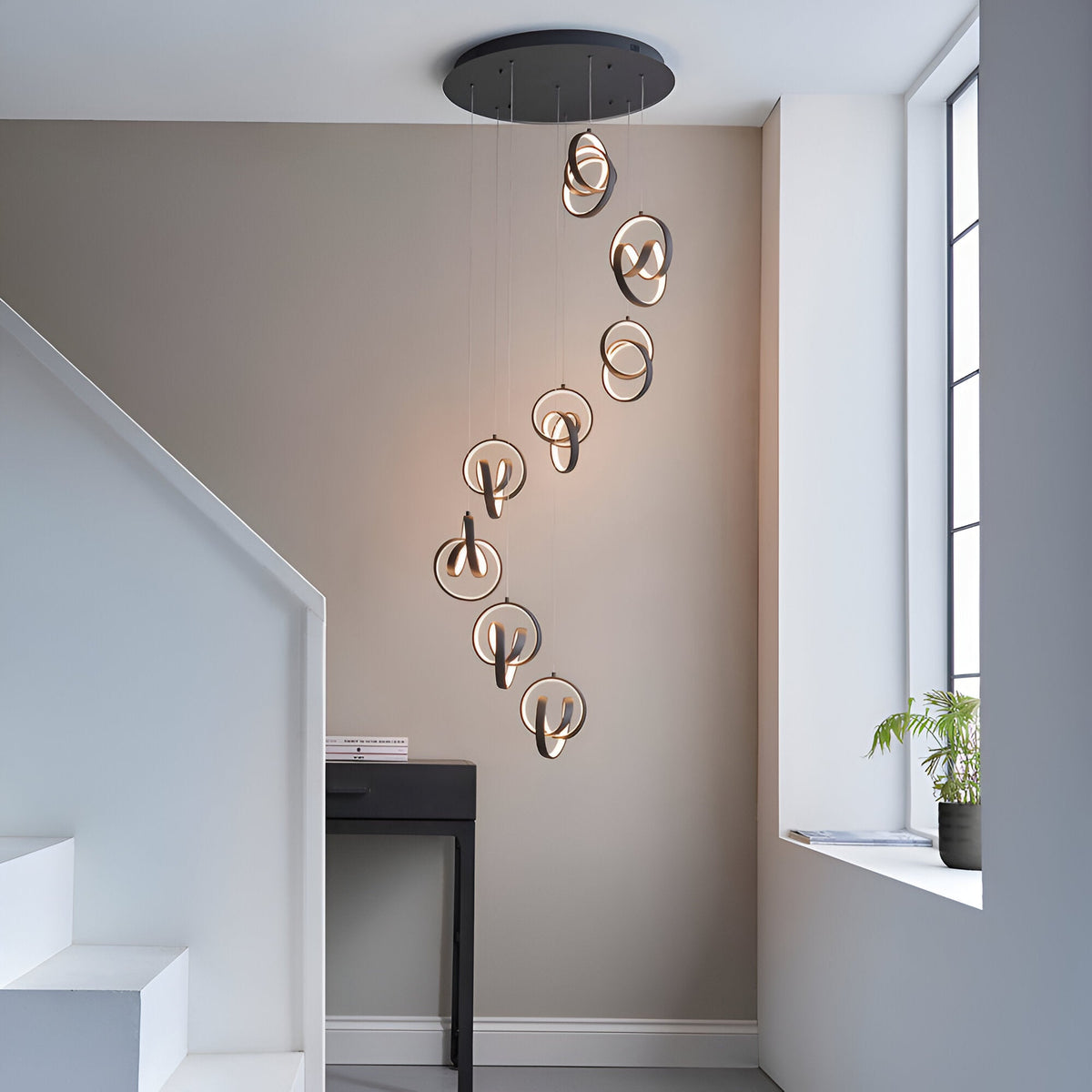 Endon Bevwell 8 light pendant in matt black, with swirling looped LED rings cascading in a spiral over a console table in a modern stairway hallway.