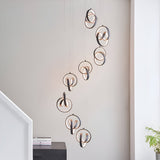 Endon Bevwell 8 light pendant in matt black, looped ring clusters cascading on clear flex in a modern stairwell with a light neutral wall.