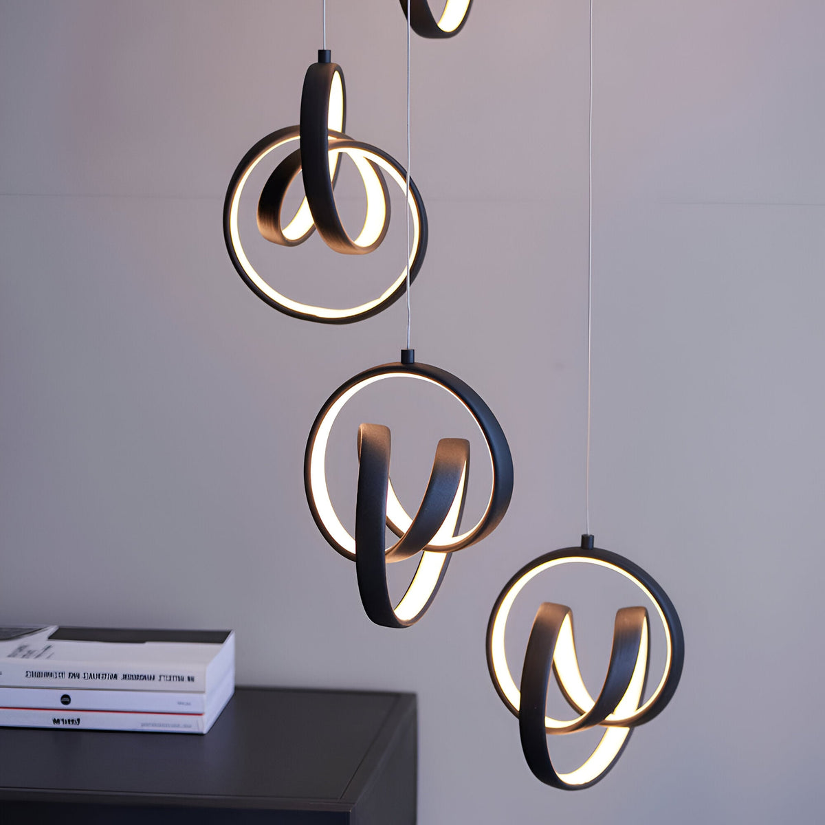 Endon Bevwell 8 light pendant in matt black with swirling looped LED rings suspended on clear flex above a dark sideboard with books.
