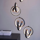 Endon Bevwell 8 light pendant in matt black with swirling looped LED rings suspended on clear flex above a dark sideboard with books.