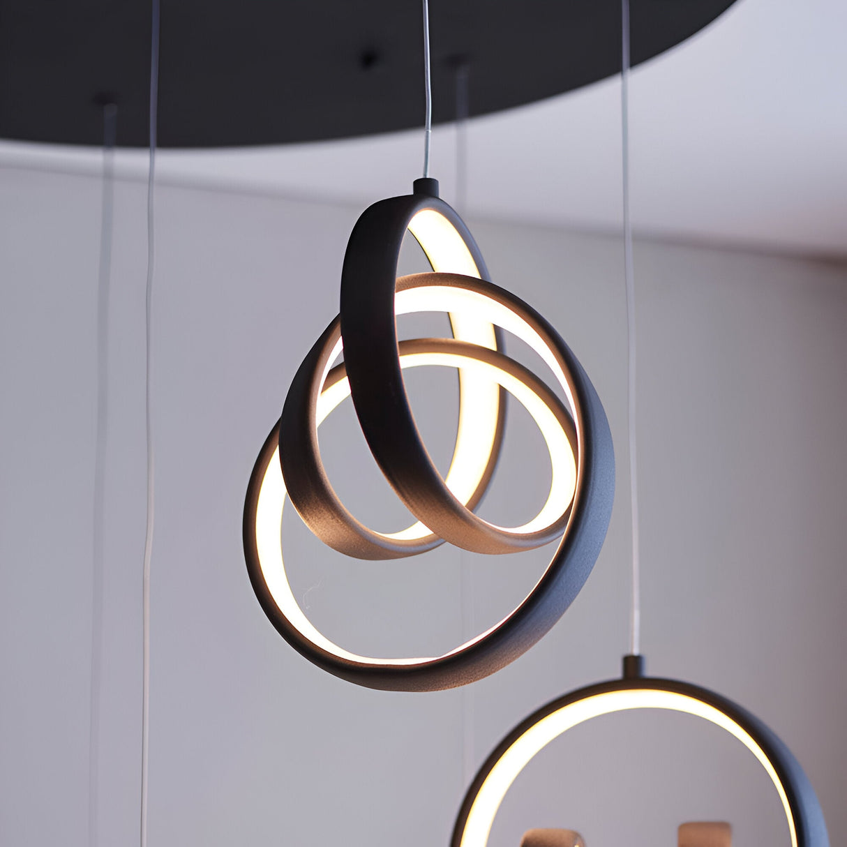 Endon Bevwell 8 light pendant in matt black, with looped metal rings clustered into a sculptural form glowing warm white, shown alongside a second pendant.