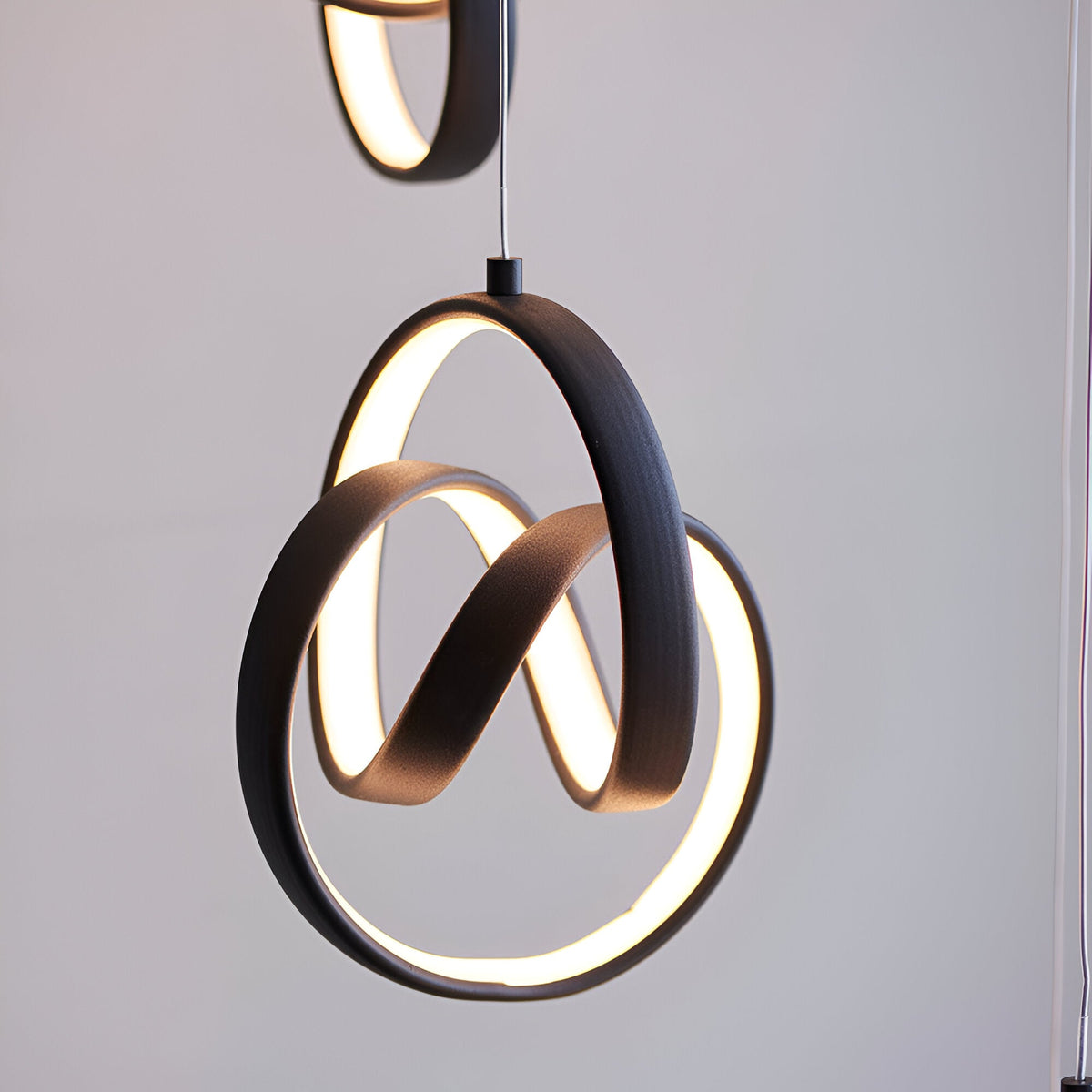 Endon Bevwell pendant light in matt black, showing looped metal rings with integrated warm LED strips against a pale grey background.