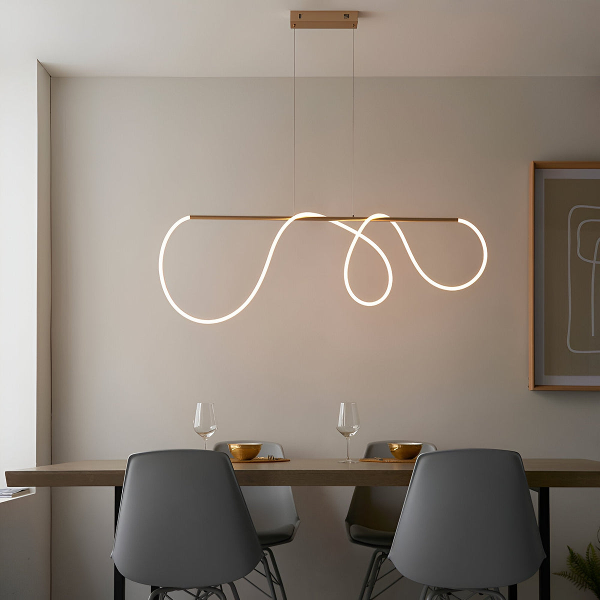Aldley Linear Pendant in satin gold with a flexible LED tube curved into loose waves, hung above a dining table with grey chairs.