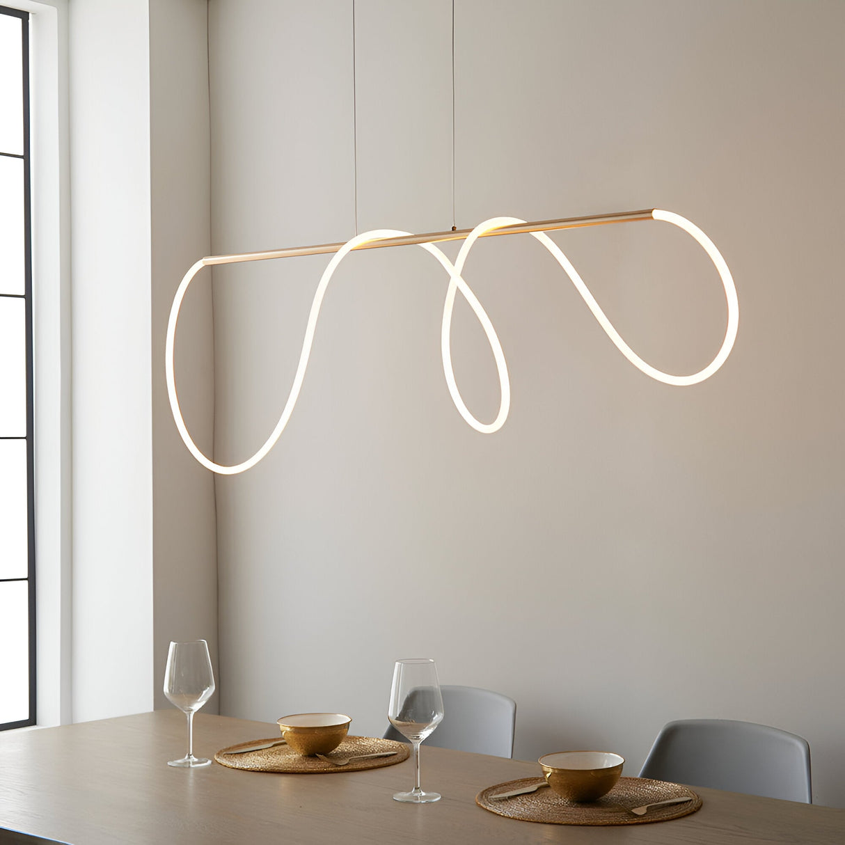 Aldley Linear Pendant in satin gold with a flexible looped LED tube, hung above a dining table in a neutral-toned room.