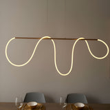 Aldley Linear Pendant in satin gold, a horizontal bar with a flexible LED tube curving into wave shapes, hung above a dining table with grey chairs.