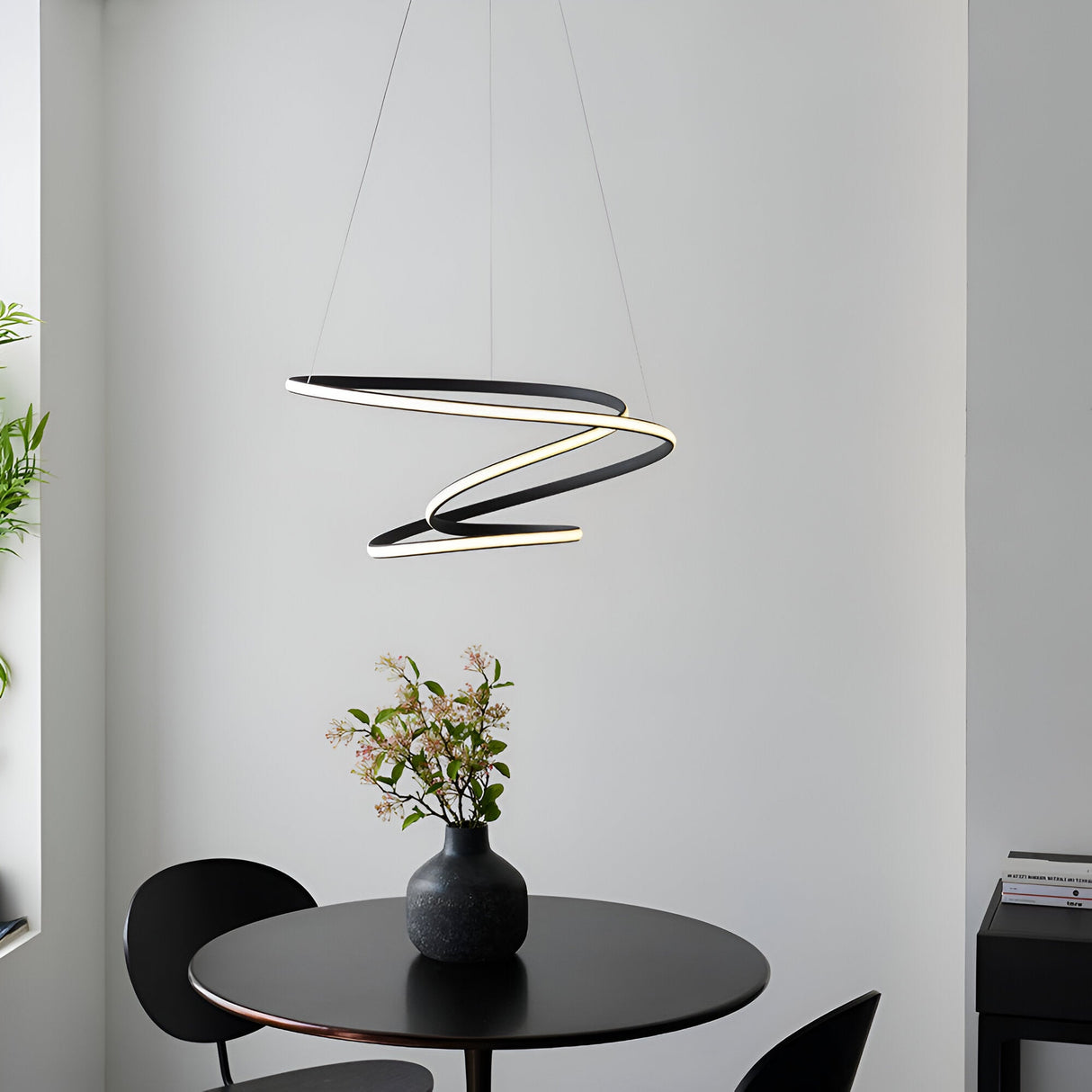 Endon Halden pendant light in textured black, formed as a looping ribbon-style LED fixture, suspended above a round black dining table in a modern interior.