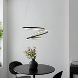 Endon Halden pendant light in textured black, formed as a looping ribbon-style LED fixture, suspended above a round black dining table in a modern interior.