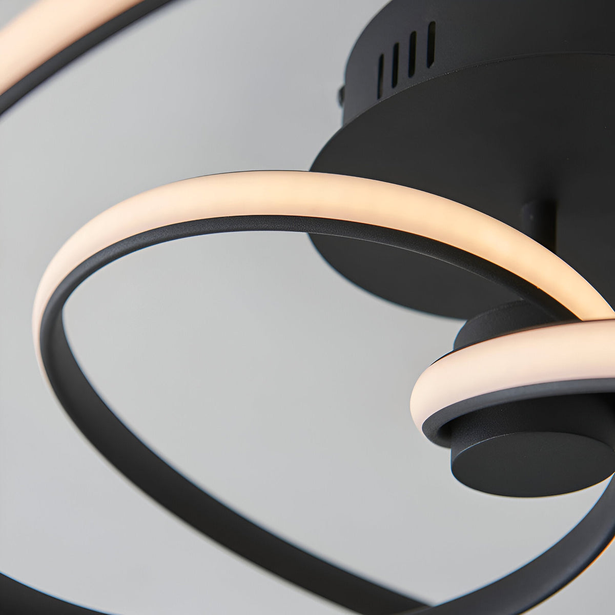 Close-up of the Endon Halden LED semi-flush ceiling light showing curved illuminated loops against a matt black metal frame and vented housing.