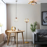 Brenmere Pendant Light with open hoop frame in brushed brass, copper and nickel, hung above a dining table alongside matching floor and table lamps.