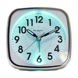 Square white plastic alarm clock with silver trim, black Arabic numerals, sweep second hand, and glowing turquoise backlight, shown on a plain background.