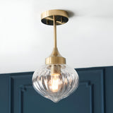 Endon Aldridge semi-flush ceiling light in antique brass with a ribbed clear glass teardrop shade, mounted below a white ceiling by a dark blue panelled wall.