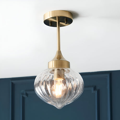 Endon Aldridge semi-flush ceiling light in antique brass with a ribbed clear glass teardrop shade, mounted below a white ceiling by a dark blue panelled wall.
