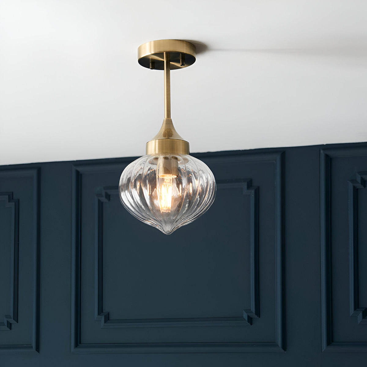 Endon Aldridge semi-flush ceiling light in antique brass with a ribbed clear glass teardrop shade, mounted below a white ceiling against navy panelling.