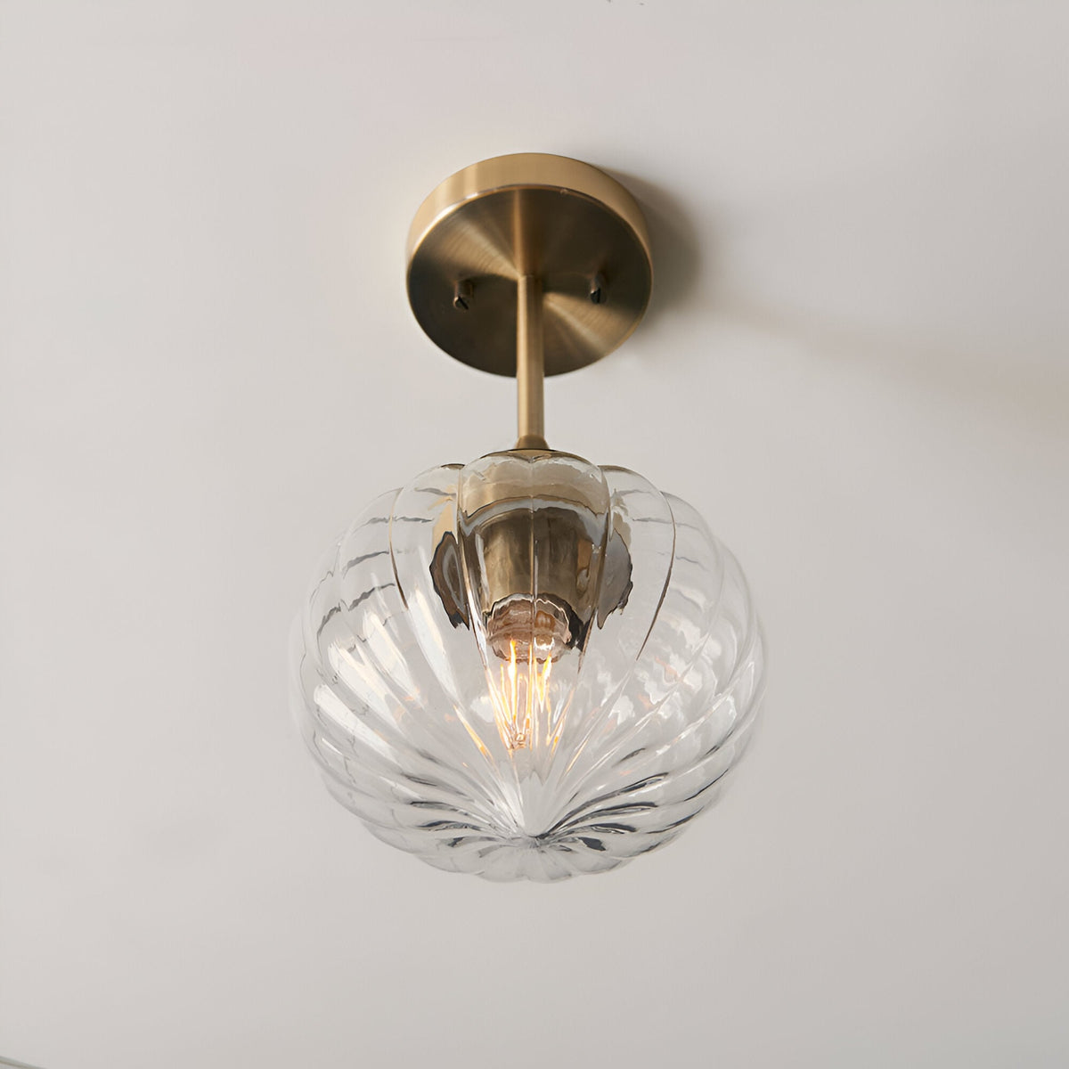 Endon Aldridge semi-flush ceiling light in antique brass with a ribbed clear glass globe shade and short brass stem, mounted on a pale ceiling.
