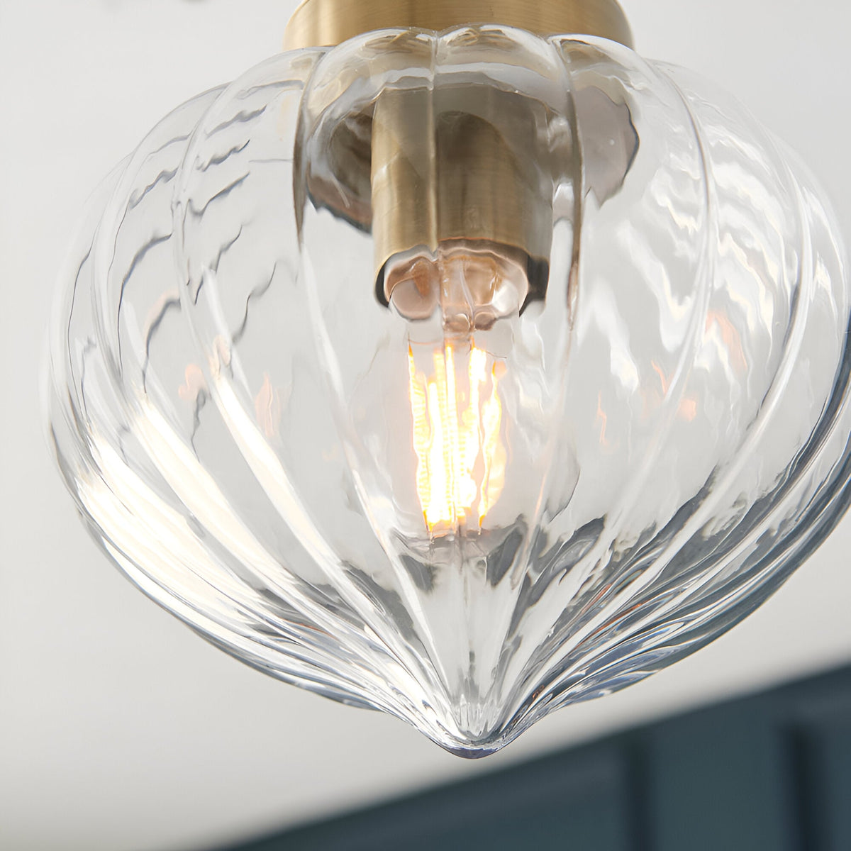 Close-up of the Endon Aldridge semi-flush ceiling light showing its ribbed clear glass shade, antique brass fitting, and illuminated E27 filament lamp.
