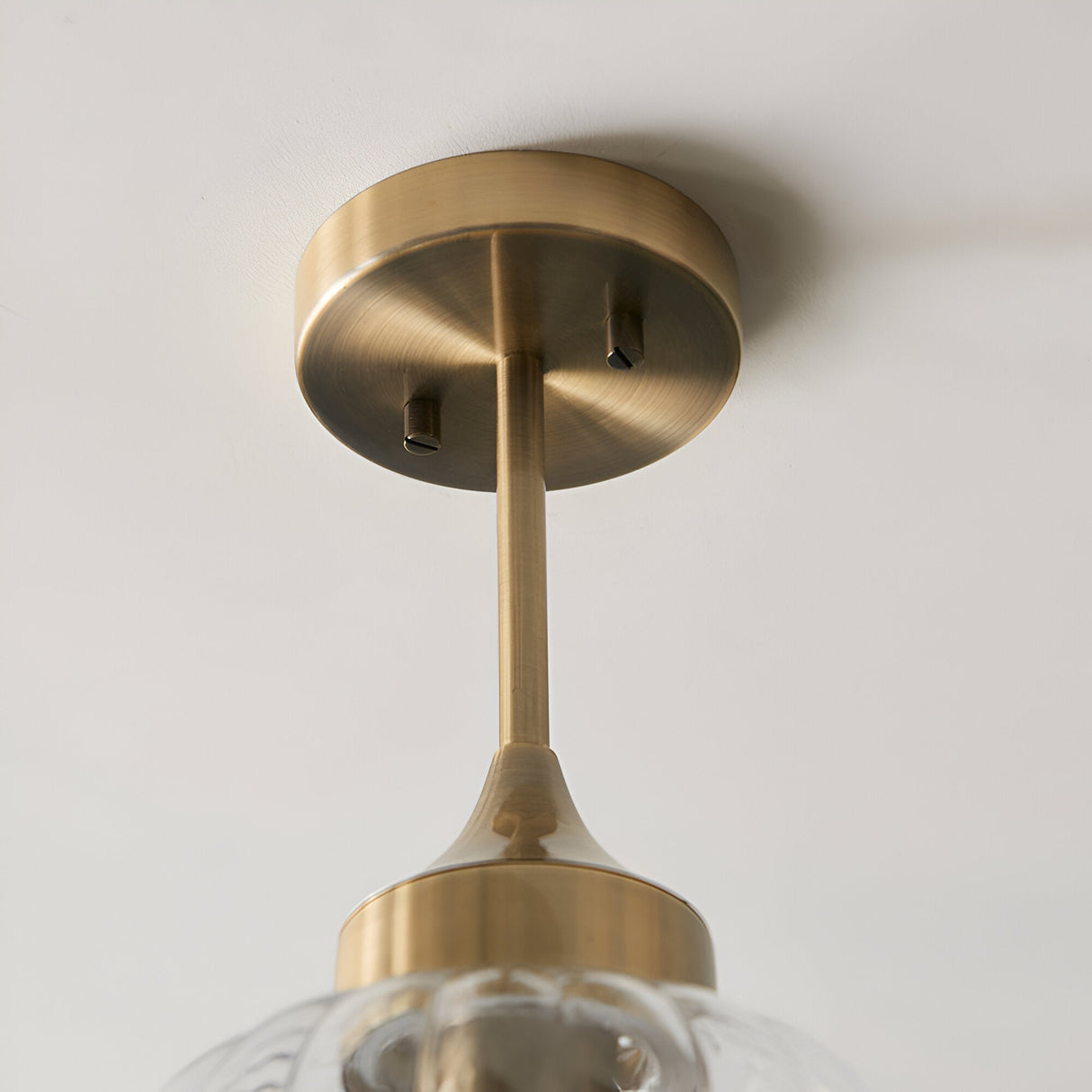 Close-up of Endon Aldridge semi-flush ceiling light showing the antique brass canopy, slim drop rod, and tapered fitting above a clear glass shade.