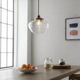 Kedleston Pendant in brass with a clear rounded glass shade, hanging above a wooden dining table in a kitchen setting.