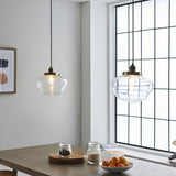 Kedleston Pendant in brass and clear glass with a schoolhouse-shaped shade, hanging above a dining table near a window in a bright kitchen.