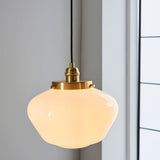 Endon Kedleston pendant light with brass fitting, opal glass schoolhouse shade and black fabric flex, hanging beside a white panelled window.