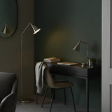 Endon Brackley nickel floor lamp with adjustable arm and conical shade beside a black desk and chair in a dark green bedroom workspace.