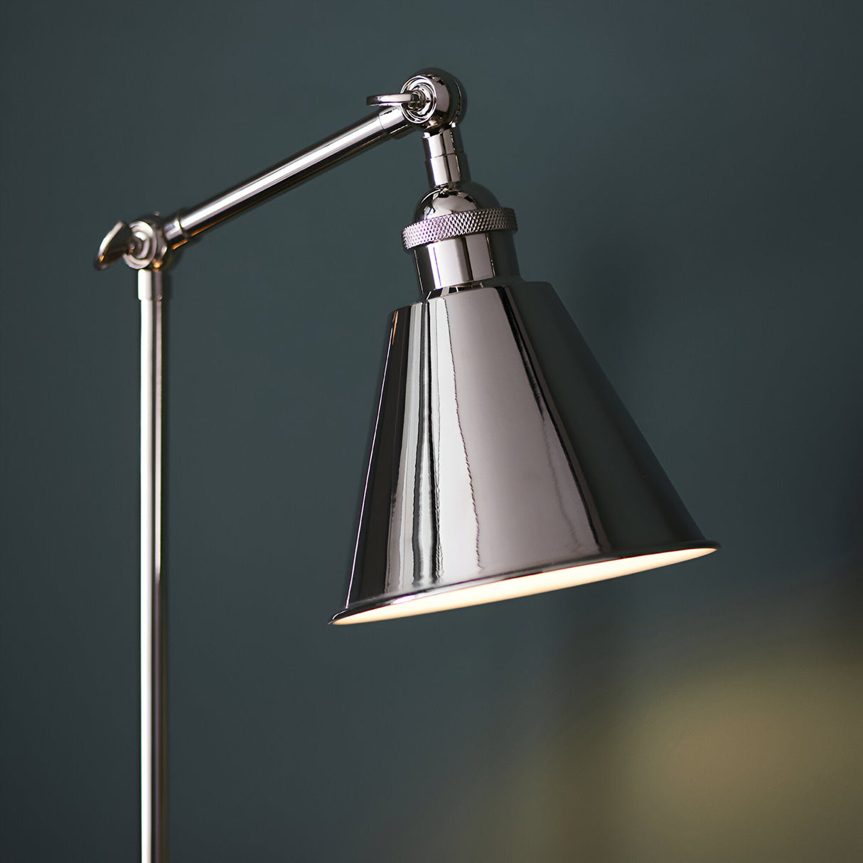 Endon Brackley table lamp in bright nickel with knurled detailing, adjustable arm and conical shade, lit against a dark teal background.