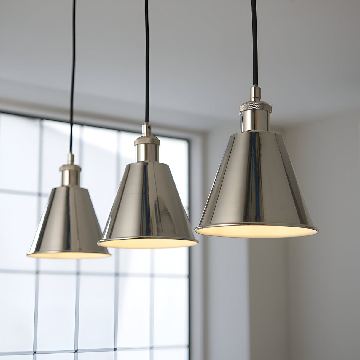 Endon Brackley 3 light linear pendant with bright nickel conical shades and white inner, hung on black flex against a bright window.