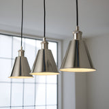 Endon Brackley 3 light linear pendant with bright nickel conical shades and white inner, hung on black flex against a bright window.