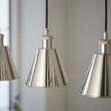 Close-up of Endon Brackley pendant lights with polished nickel conical shades, knurled detailing, and black fabric flex against a pale wall.
